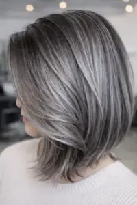 Side view of a person with shoulder-length gray blended hair in a layered bob, showing silver and dark strands.