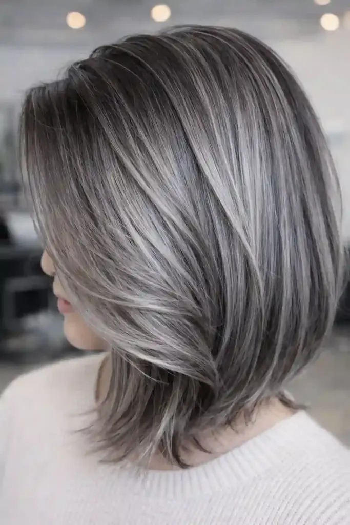 Side view of a person with shoulder-length gray blended hair in a layered bob, showing silver and dark strands.