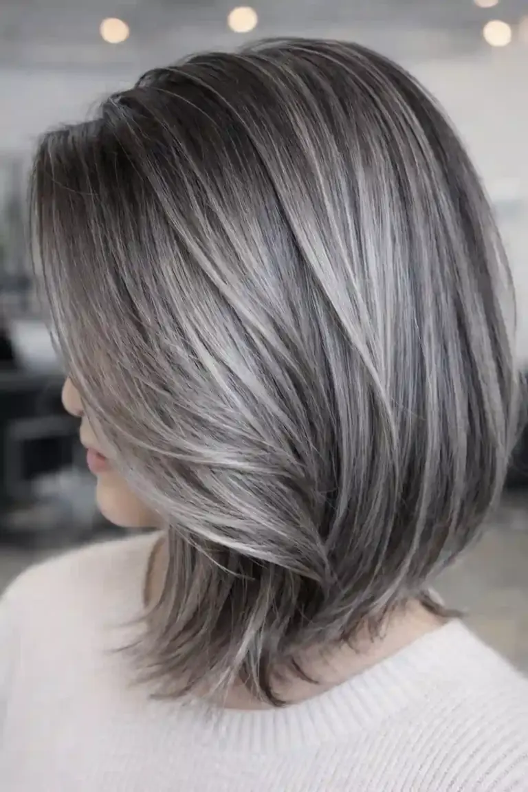 Side view of a person with shoulder-length gray blended hair in a layered bob, showing silver and dark strands.