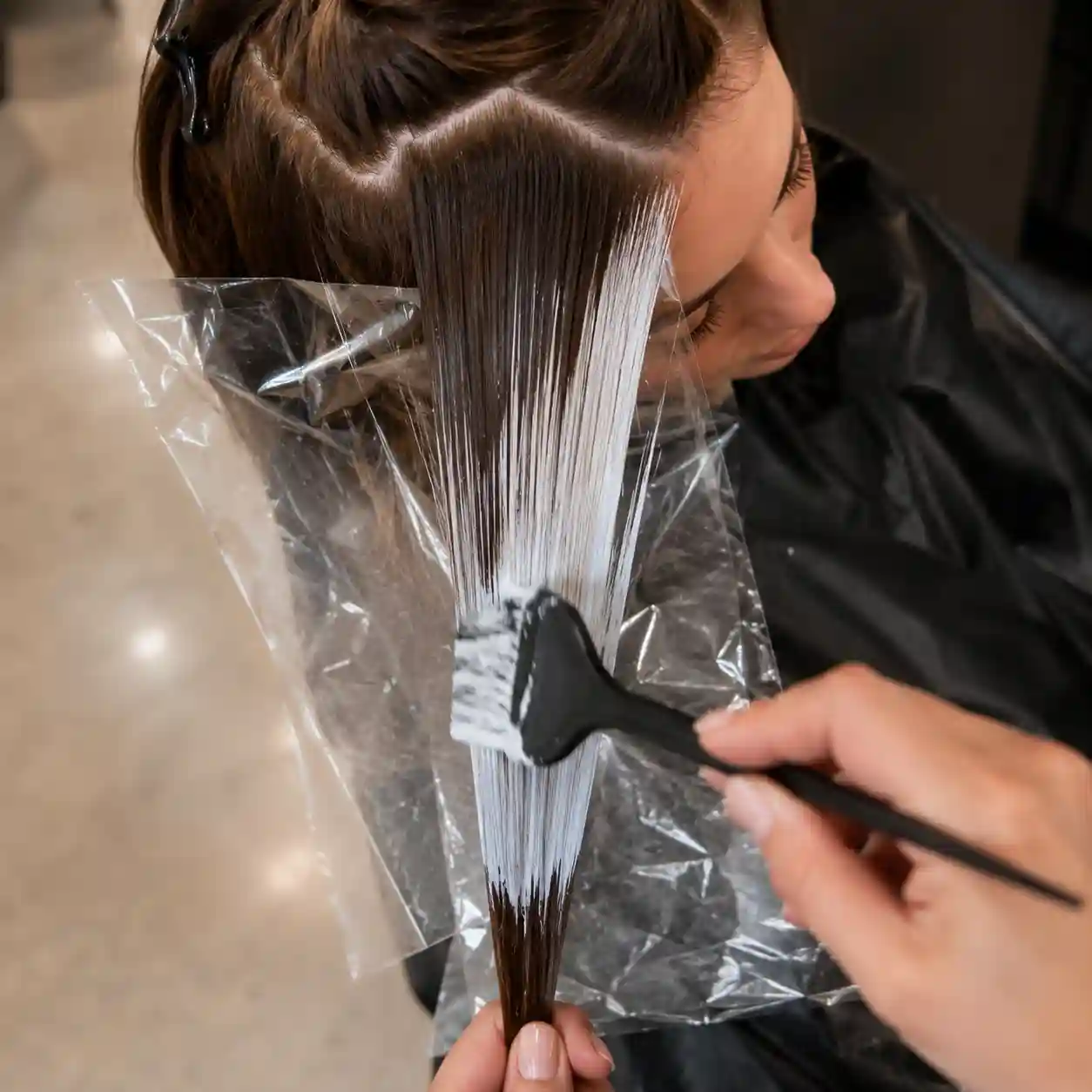Hair colorist hand-painting lightener onto sections of medium brown hair during a balayage service at Studio 303 in Englewood, CO.